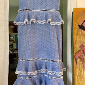 May include: A light blue midi dress with white lace trim and multiple tiers. The dress has a square neckline and thin straps.
