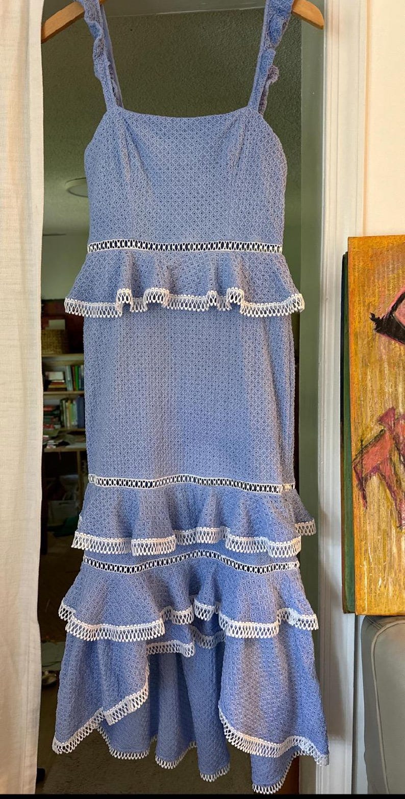 May include: A light blue midi dress with white lace trim and multiple tiers. The dress has a square neckline and thin straps.