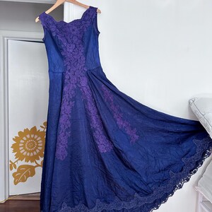 May include: A long, blue, sleeveless dress with purple lace detailing. The dress has a scoop neckline and a full skirt.