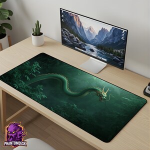 Könnte beinhalten: Rechteckige Schreibtischunterlage mit einem grünen Drachendesign in einem Wald. Der Drache steht im Mittelpunkt, umgeben von grünem Laub. Die Unterlage liegt auf einem Holztisch, mit einem Computermonitor und einem kleinen Kaktus im Hintergrund. Das PhantomDesk-Logo ist sichtbar.