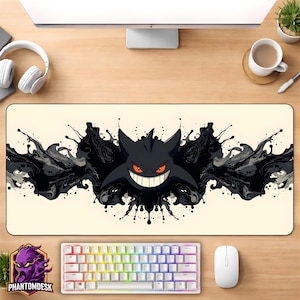 May include: A rectangular desk mat with a black cartoon character with a wide grin and red eyes, set against a backdrop of black ink-like splatters. A white keyboard and mouse are visible below the mat. The PhantomDesk logo is in the lower left corner.