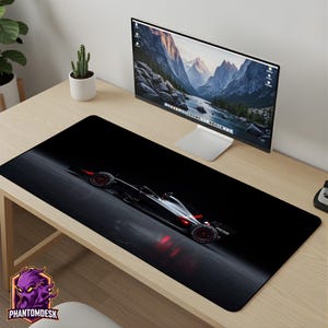 May include: A rectangular desk mat featuring a high-contrast graphic of a black and silver Formula 1 race car on a dark, reflective surface. The car design includes red accents on the wheels and rear wing, set against a deep black background.