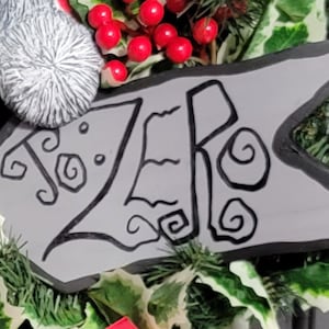 May include: A gray and black Christmas wreath with a white skull and a sign that says "Zero" in a black, stylized font.