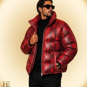 May include: A red puffer jacket featuring a snakeskin pattern, a high collar, and a front zipper closure. The jacket is worn over a black turtleneck sweater and black trousers, paired with dark sunglasses and a gold wristwatch on the wrist.