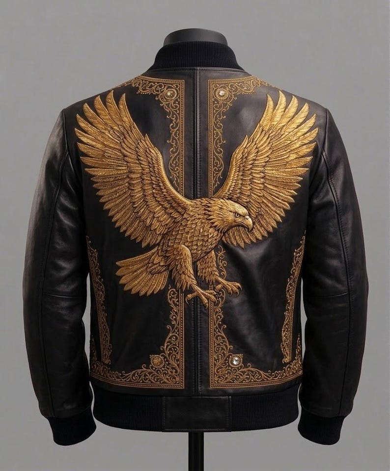 May include: A black leather bomber jacket featuring a large, detailed gold embroidered eagle on the back. The design includes intricate gold filigree patterns framing the eagle, with small circular accents integrated into the decorative borders.
