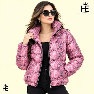 Könnte beinhalten: Eine pink-schwarze Steppjacke mit Schlangenmuster, hohem Kragen und durchgehendem Frontreißverschluss. Die Jacke wird über einem schwarzen Oberteil und einer schwarzen Hose getragen. Das HE-Logo mit Kronensymbol ist in den Ecken zu sehen.