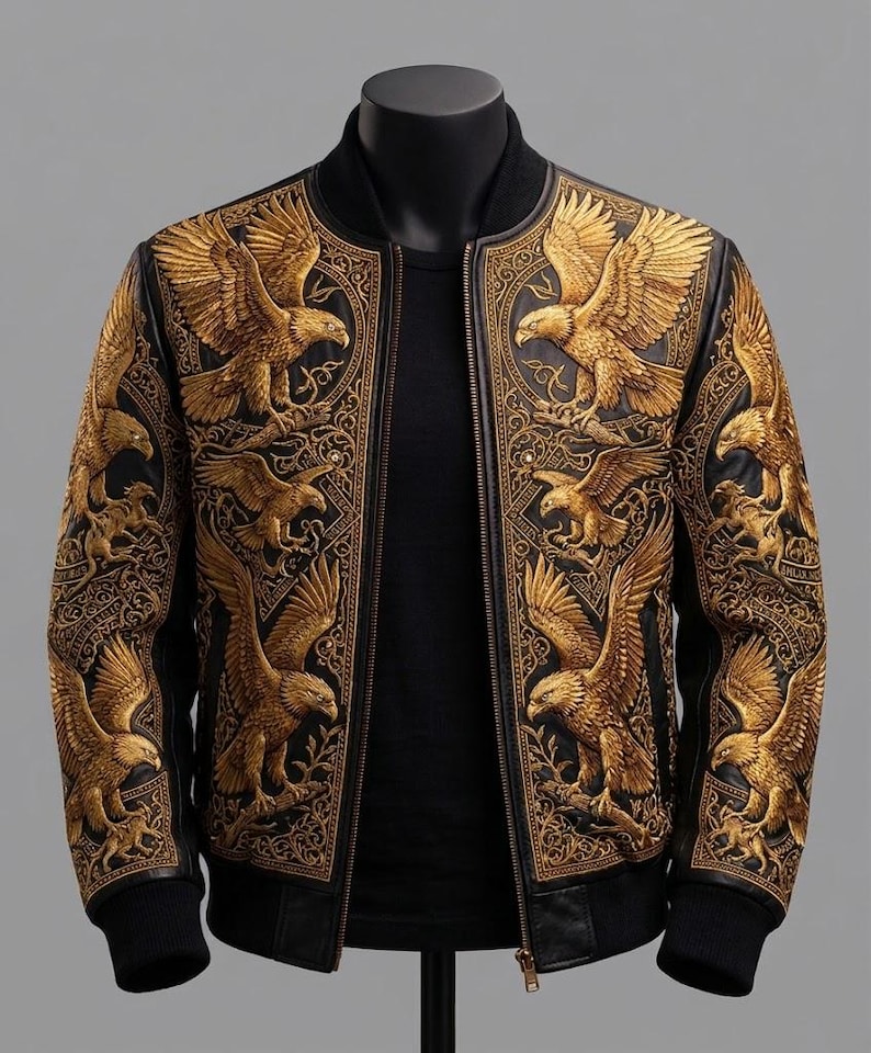 May include: A black bomber jacket featuring intricate gold-colored embroidery of eagles and ornate scrollwork patterns across the front panels and sleeves. The jacket has a ribbed black collar, cuffs, and hem, with a central front zipper closure.