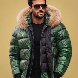 Könnte beinhalten: Eine Daunenjacke mit grün-schwarzem Schlangenledermuster, einer großen Kapuze mit beigem Kunstfellbesatz, schwarzem Innenfutter, Frontreißverschluss und schwarzen Rippbündchen, getragen über einem schlichten schwarzen Oberteil und einer schwarzen Hose.