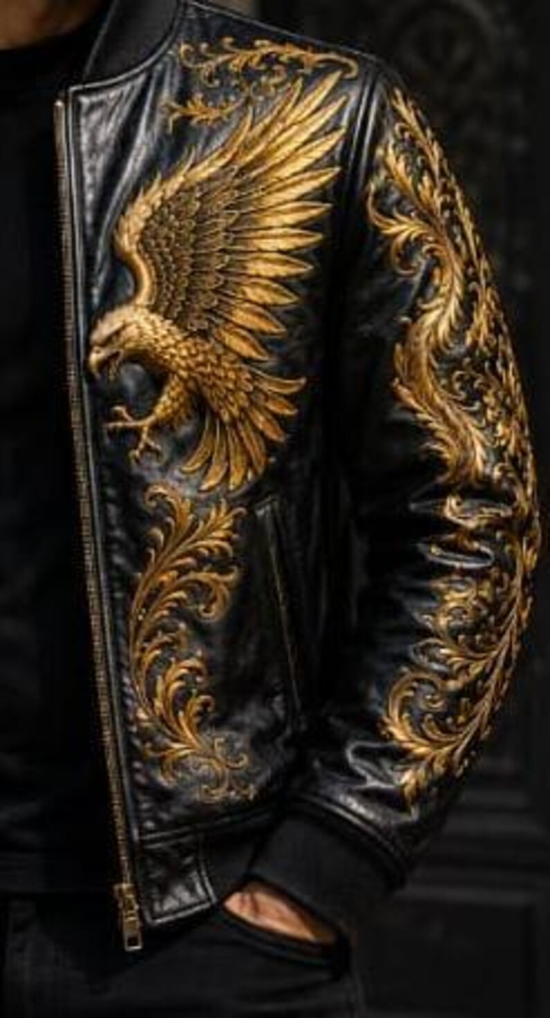 May include: A black leather bomber jacket featuring intricate gold embroidery. The design includes a large eagle on the chest and detailed scrolling floral patterns extending across the shoulder and down the sleeve, finished with a gold zipper.