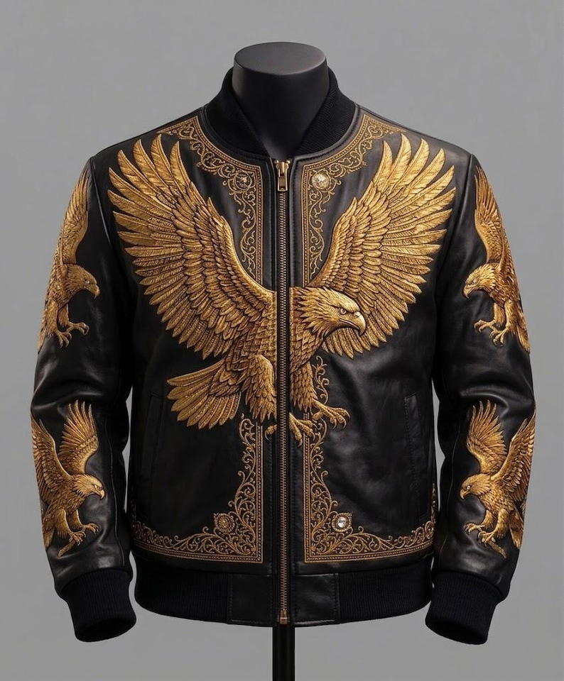 May include: A black leather bomber jacket featuring intricate gold embroidery of a large eagle across the chest and smaller eagles on each sleeve. The design includes ornate gold filigree patterns along the front zipper and collar area.