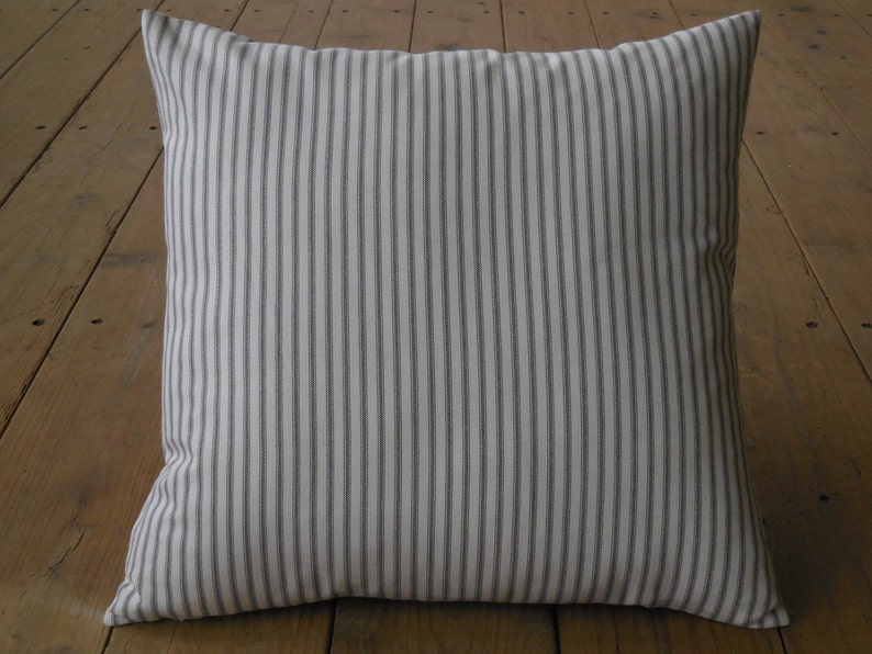 May include: A white cushion with thin grey stripes. The cushion is square and has a soft, textured fabric.