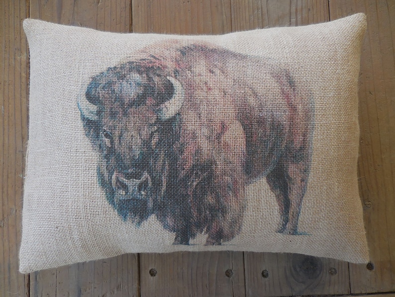 May include: A brown and black buffalo printed on a beige burlap pillow. The pillow is a throw pillow with a simple design.