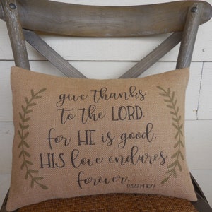 May include: A burlap pillow with a brown and green design. The pillow has the text "give thanks to the LORD. for HE is good. HIS love endures forever. PSALM 101" printed on it.