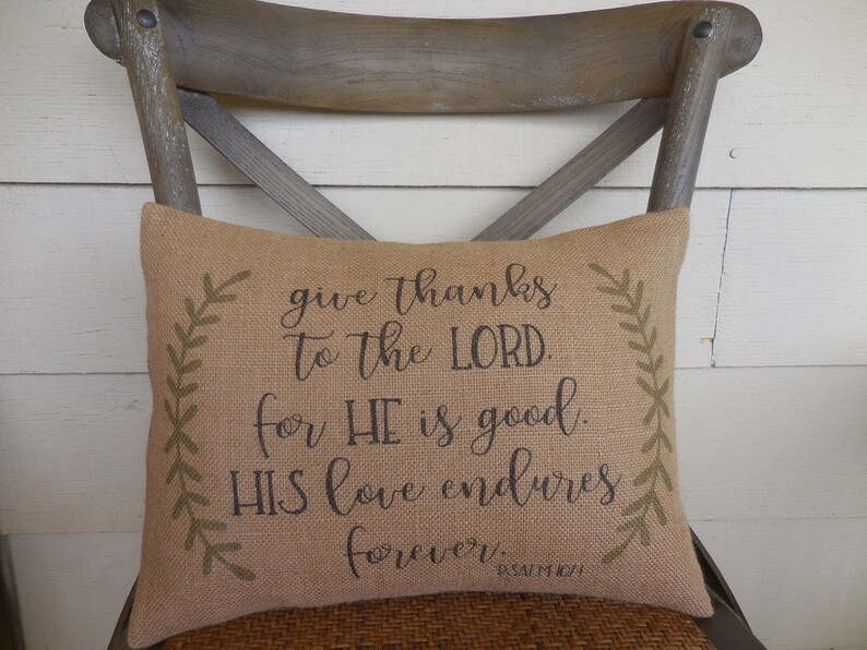 May include: A burlap pillow with a brown and green design. The pillow has the text "give thanks to the LORD. for HE is good. HIS love endures forever. PSALM 101" printed on it.