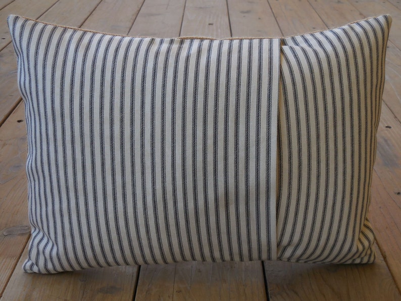 May include: A white and black striped pillow with a brown seam. The pillow is made of a soft, woven fabric.