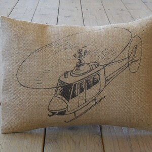 Puede incluir: Una almohada de arpillera marrón con una ilustración en blanco y negro de un helicóptero.