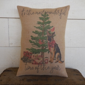 May include: A burlap pillow with a printed design of a German Shepherd dog standing next to a Christmas tree. The text "It's the most wonderful time of the year" is printed on the pillow.
