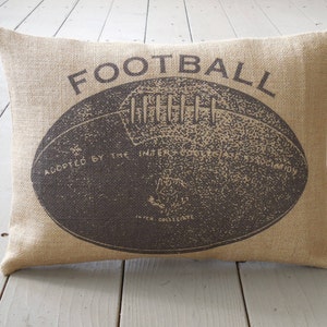 May include: A brown burlap pillow with the word "FOOTBALL" printed in black. The pillow features a vintage illustration of a football with the text "Adopted by the Intercollegiate Football Association" printed on the ball.