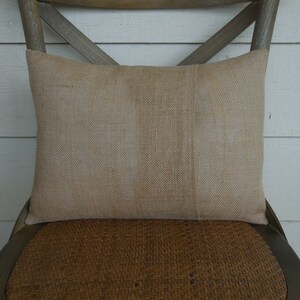 May include: A natural burlap pillow with a subtle striped pattern. The pillow is placed on a woven chair seat.