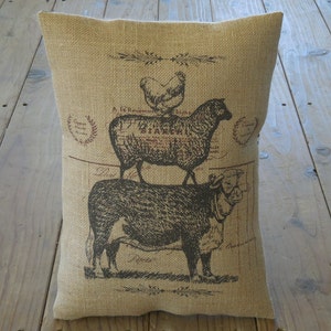 May include: A burlap pillow with a vintage-style print of a chicken, sheep, and cow stacked on top of each other. The print is in brown and black on a beige background.