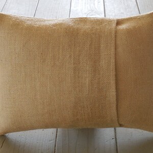 May include: A tan burlap pillow with a seam down the center. The pillow is made of a rough, textured fabric.