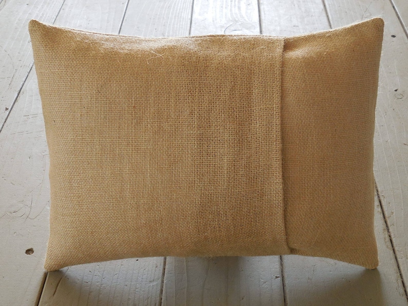 May include: A tan burlap pillow with a seam down the center. The pillow is made of a rough, textured fabric.
