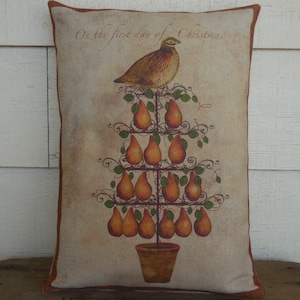 May include: A decorative pillow with a vintage-style illustration of a pear tree with a quail perched on top. The tree is decorated with brown pears and green leaves. The text "On the first day of Christmas" is printed at the top of the pillow.