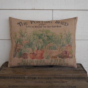 May include: A burlap pillow with a printed image of potted plants and the text "The Potting Shed, Life is Better in the Garden, Seedlings - Bulbs, Herbs Potted Plants".