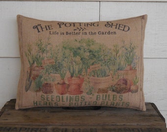 May include: A burlap cushion with a printed image of potted plants and the text "The Potting Shed, Life is Better in the Garden, Seedlings - Bulbs, Herbs Potted Plants".
