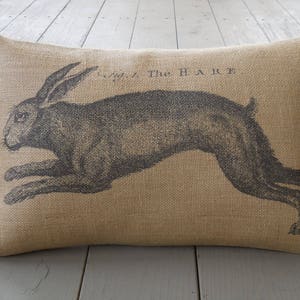 May include: A burlap pillow with a black and white illustration of a hare running. The pillow has the text "The Hare" printed on it.