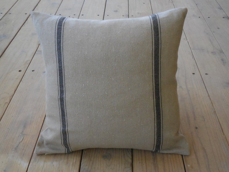 May include: A beige linen pillow with black stripes. The pillow is made of a soft, natural fabric and has a simple, elegant design.