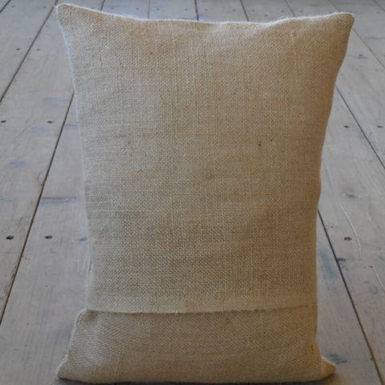 May include: A natural-colored burlap pillow with a simple, rectangular shape. The pillow is made of a coarse, woven fabric with a slightly textured surface.