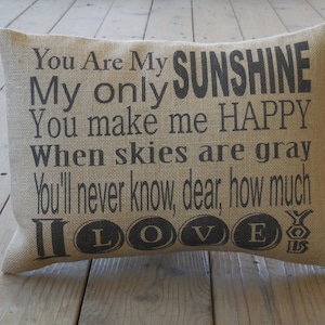 May include: A burlap pillow with the text "You Are My SUNSHINE My only You make me HAPPY When skies are gray You'll never know, dear, how much I LOVE YOU" printed in black.