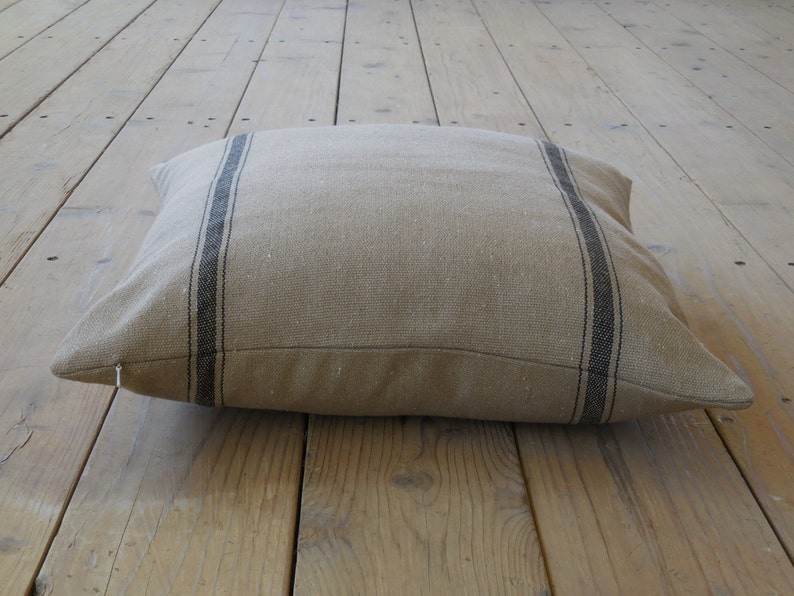 May include: A large, rectangular floor cushion with a beige linen fabric and black stripes. The cushion is lying on a wooden floor.
