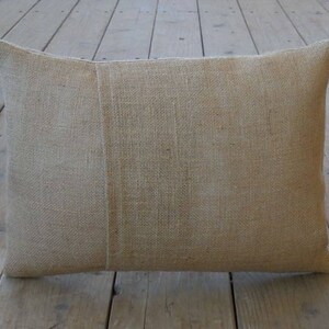May include: A natural-colored burlap pillow with a seam down the center. The pillow is made of a rough, textured fabric.