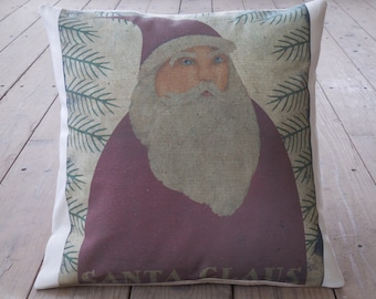 May include: A white pillow with a red and white Santa Claus illustration. The illustration features a white beard and a red hat. The background is a green and white pattern of pine branches. The text "SANTA CLAUS" is printed at the bottom of the pillow.