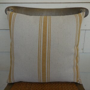 May include: A beige and mustard yellow striped throw pillow with a subtle linen texture.
