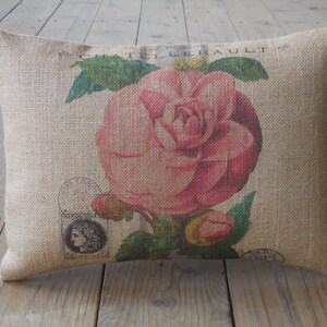 May include: A burlap pillow with a pink flower printed on it. The flower is surrounded by green leaves and the text "CHATELIERAULT" is printed on the pillow.