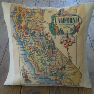 May include: A vintage-style pillow featuring a map of California with illustrations of landmarks and agricultural products. The map is surrounded by a white border and the text "CALIFORNIA" is printed in a decorative font at the top.