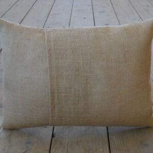 May include: A natural-colored burlap pillow with a subtle texture. The pillow is rectangular and has a seam down the center.