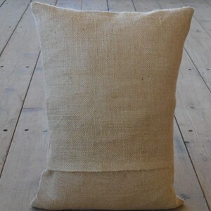May include: A natural-colored burlap pillow with a simple design. The pillow is made of a coarse, woven fabric and has a slightly textured surface.