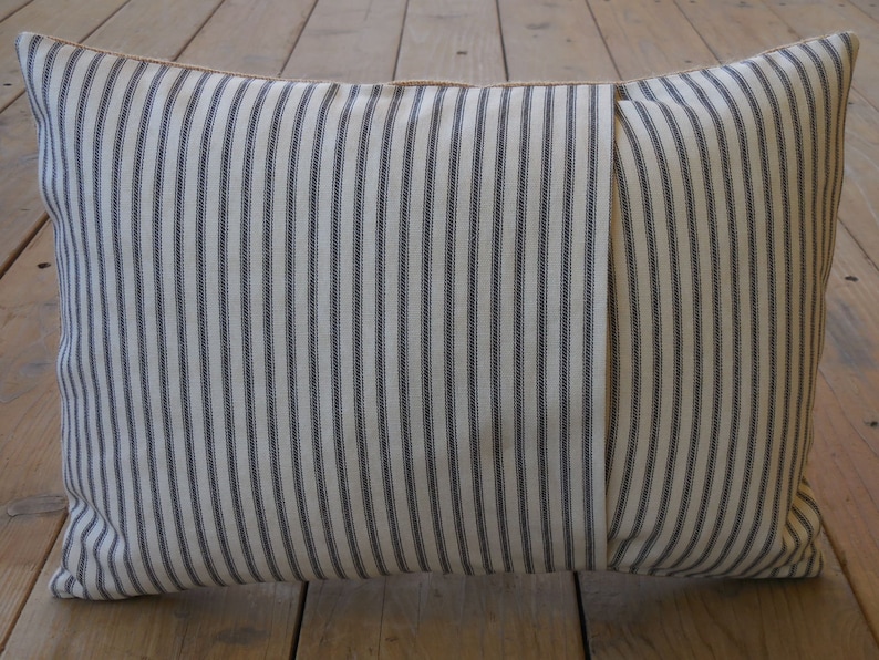 May include: A white and black striped pillow with a brown seam. The pillow is made of a soft, woven fabric.