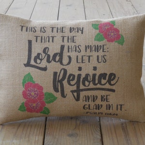 May include: A burlap pillow with a floral design and the text "This is the day that the Lord has made: Let us Rejoice and be glad in it. - Psalm 118:24"