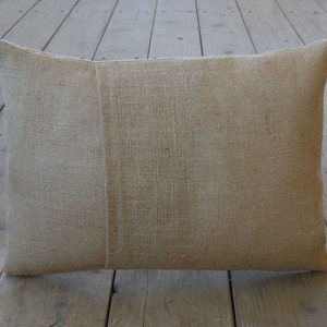 May include: A natural-colored burlap pillow with a subtle texture. The pillow is rectangular and has a seam down the center.