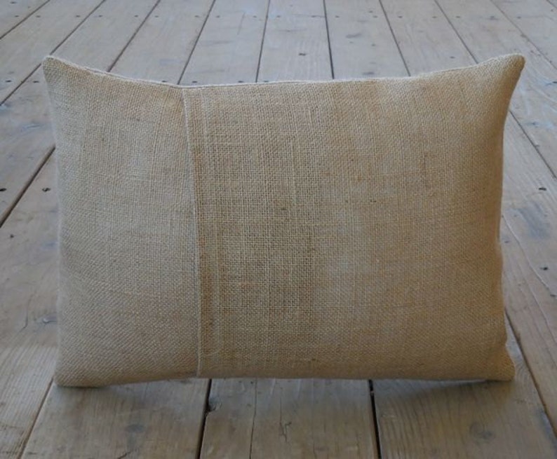 May include: A natural-colored burlap pillow with a subtle texture. The pillow is rectangular and has a seam down the center.