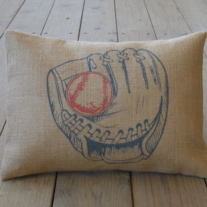May include: A brown burlap pillow with a blue and white illustration of a baseball glove catching a red baseball.