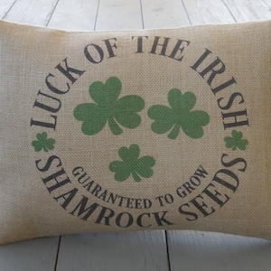 Puede incluir: Una almohada de arpillera con el texto "Luck of the Irish Shamrock Seeds Guaranteed to Grow" impreso en ella. La almohada presenta un diseño de trébol verde.