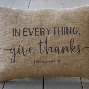 May include: A brown burlap pillow with the text "IN EVERYTHING, give thanks" and the scripture reference "1 Thessalonians 5:18" printed in black.