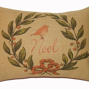 May include: A beige burlap pillow with a red bird and green leaves forming a wreath around the word "Noel".