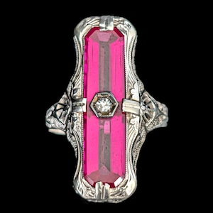 Peut inclure: Une bague vintage en argent ornée d'une grande pierre précieuse rectangulaire rose vif. La bague présente un design filigrané orné avec une petite pierre claire hexagonale au centre de la pierre rose. Sur fond noir.